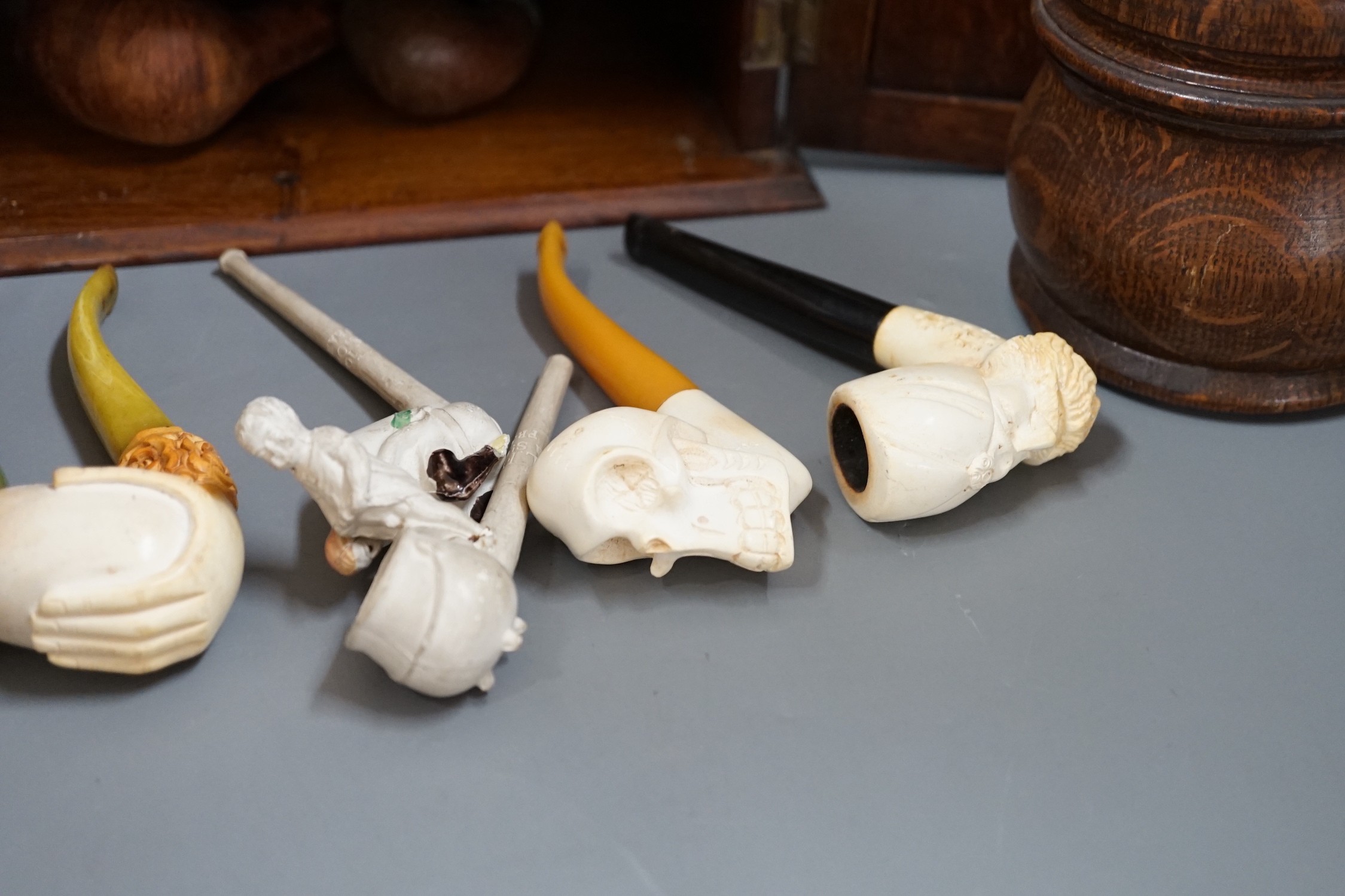 A carved smoker’s cabinet containing Meerschaum and other pipes and a tobacco jar, cabinet 25cm high